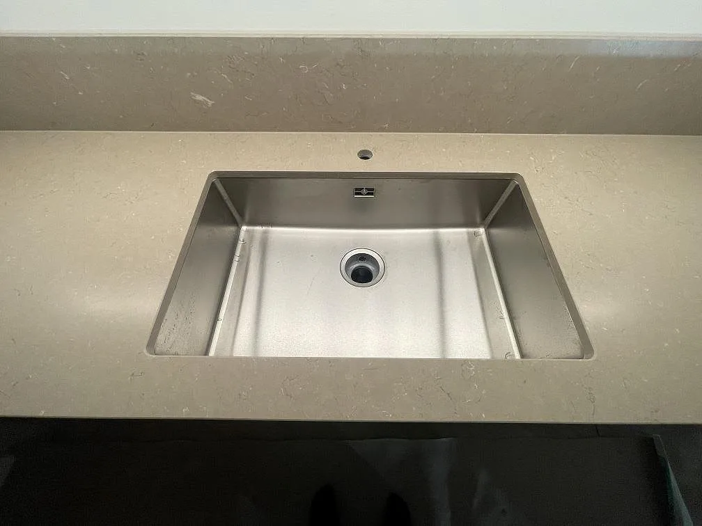 Närbild av rostfri diskho i en matt köksbänkskiva av Silestone Coral Clay med matchande stänkskydd i Uppsala.