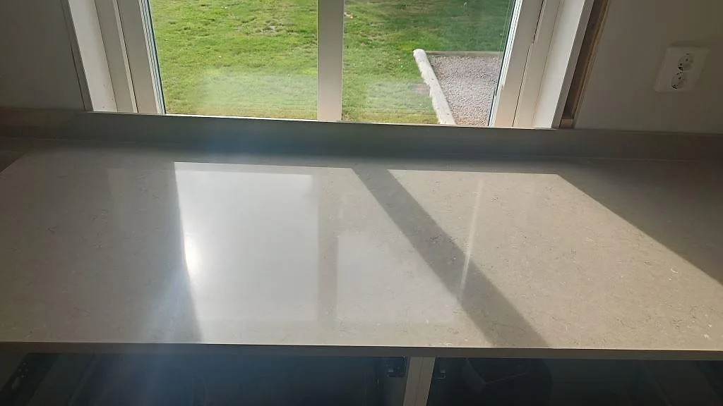 Rak bänkyta i polerad Silestone Coral Clay med fönsterreflexer och uppvikt stänkskydd i ett kök i väckelsång.