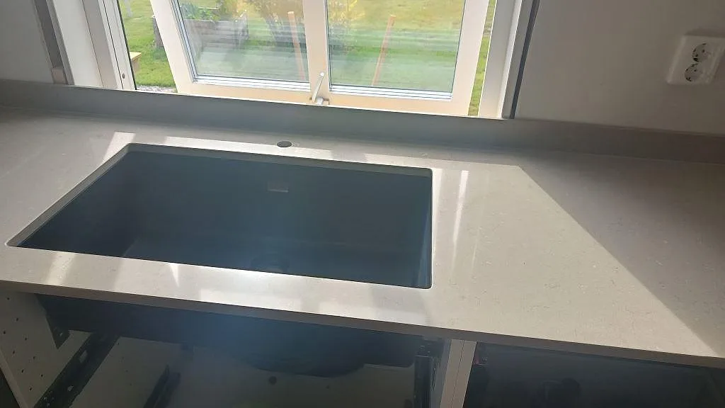 Polerad Silestone Coral Clay bänkskiva med svart diskho, blandarhål och låg stänkkant framför fönster i väckelsång.