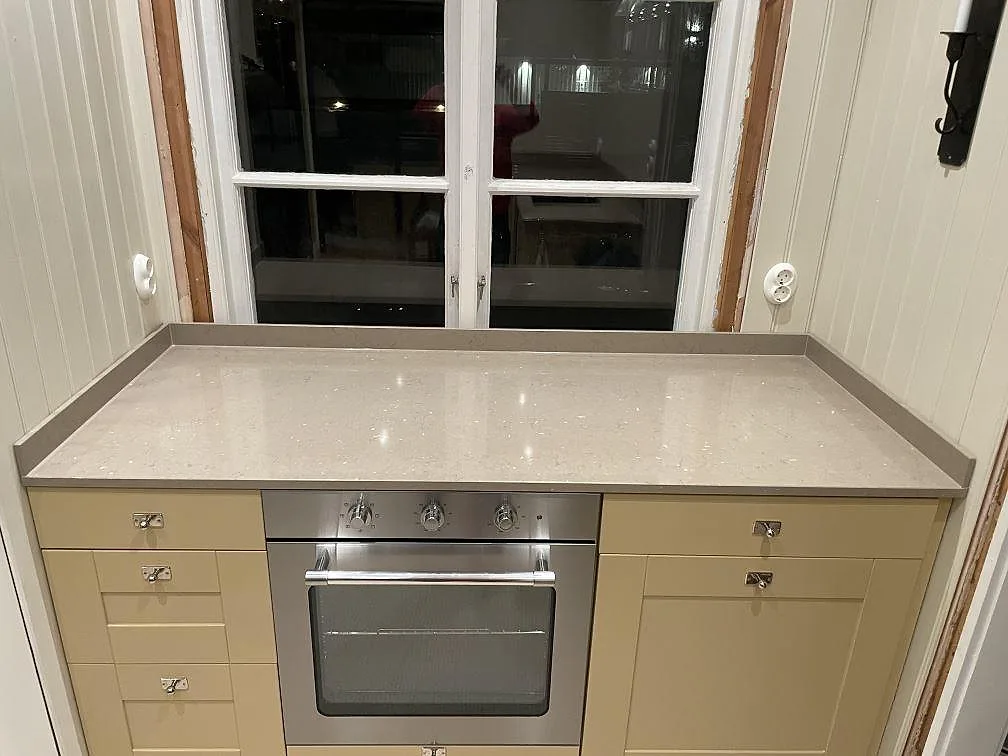Köksbänkskiva i beige Silestone Coral Clay, polerad, monterad i en fönsterrad ovanför en inbyggnadsugn i ett kök i Västerås.