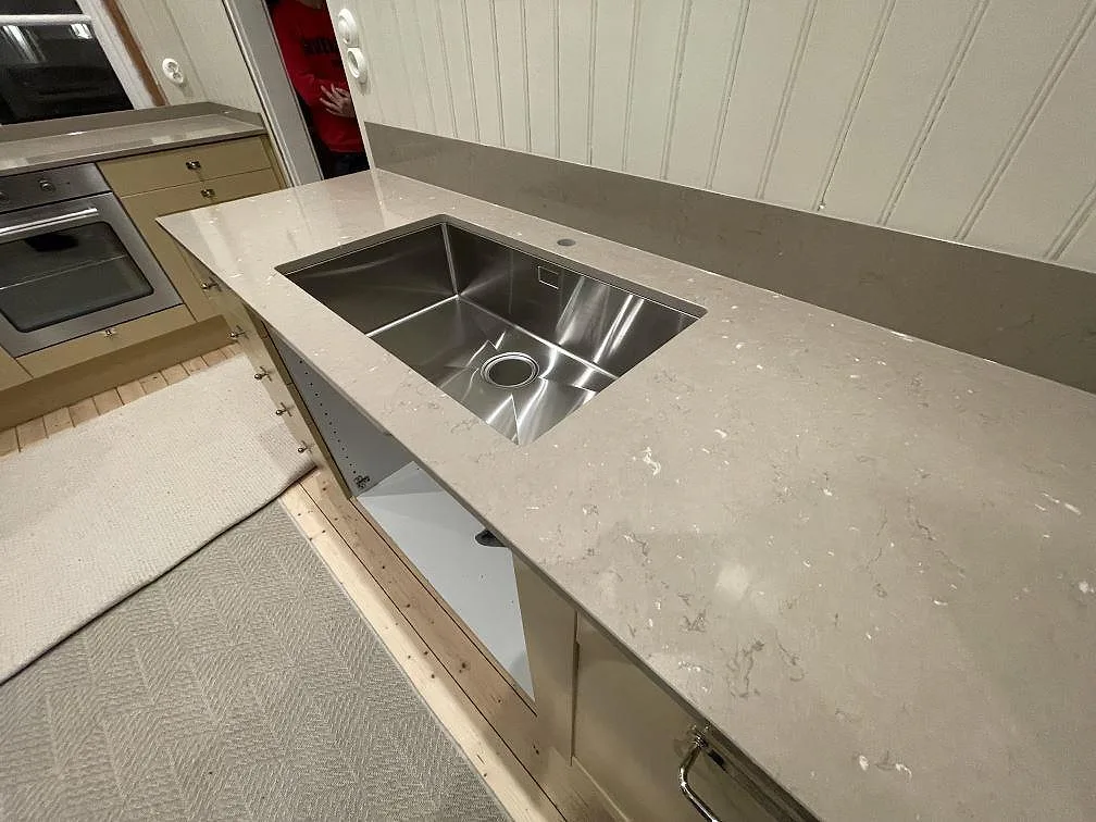 Underlimmad rostfri diskho i en beige Silestone Coral Clay bänkskiva sedd snett, kök under montering i Västerås.