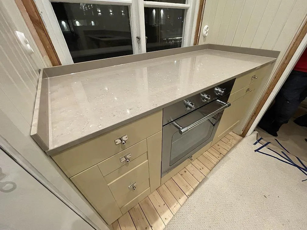 Beige Silestone Coral Clay köksbänkskiva med gerad framkant och inbyggnadsugn vid fönstret i ett kök i Västerås.