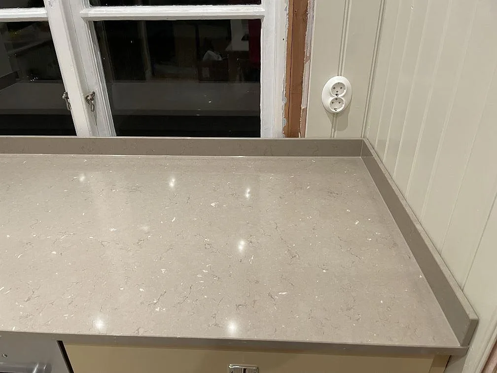 Polerad framkant och yta på en Silestone Coral Clay bänkskiva vid ett köksfönster i Västerås, med diskret ådring.