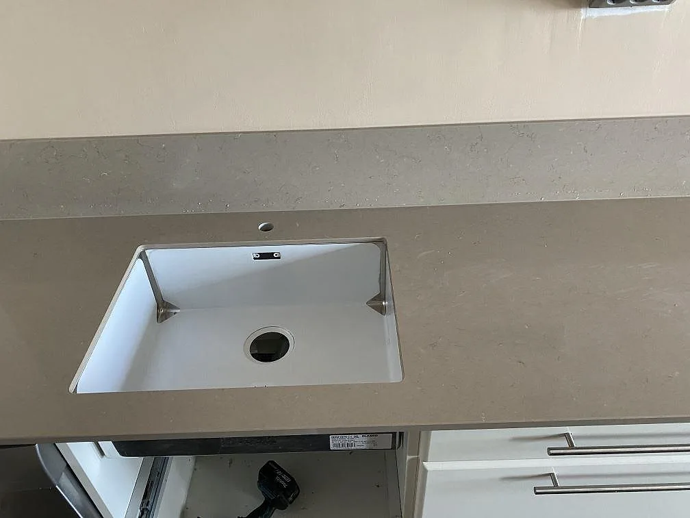 Underlimmad vit diskho i en köksbänkskiva av Silestone Coral Clay med borrat blandarhål, polerad kvartskomposit i Västra Frölunda.