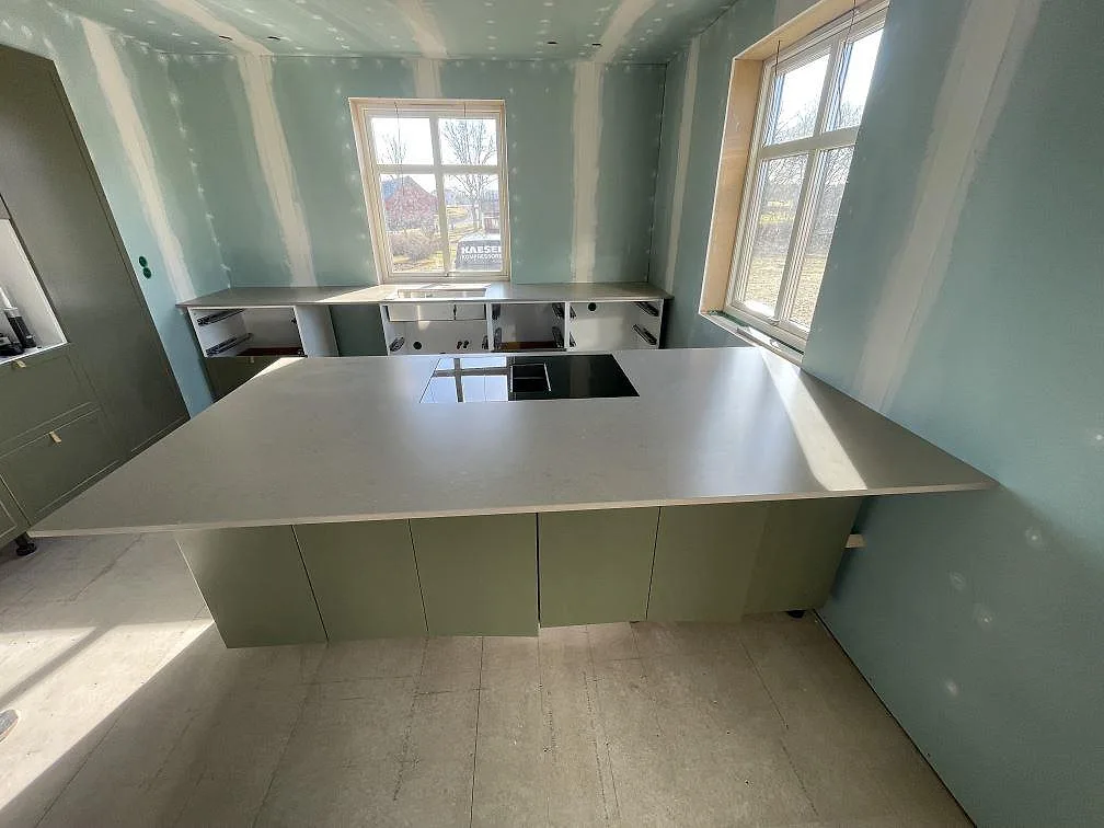 U-format kök i Vaggeryd med köksbänkskiva och stor köksö i Silestone Coral Clay, varm beige kvartskomposit med matt finish och infälld induktionshäll.
