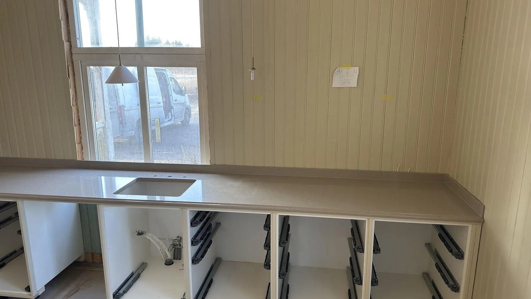Lång bänkrad i beige Silestone Coral Clay komposit med undermonterad diskho och öppna stommar i ett kök under montering i Valla, Katrineholm.