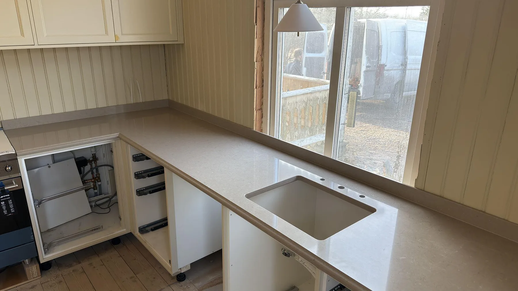 Polerad köksbänkskiva i Silestone Coral Clay med undermonterad diskho vid fönstret och uppvikt stänkkant i ett kök i Valla, Katrineholm.