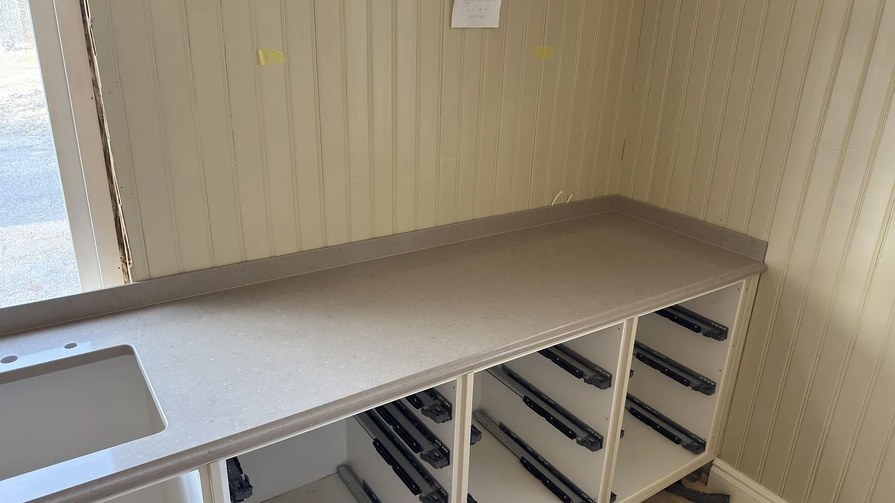 Köksbänkskiva i polerad Silestone Coral Clay med diskho och öppna lådstommar längs väggen i ett kök i Valla, Katrineholm.