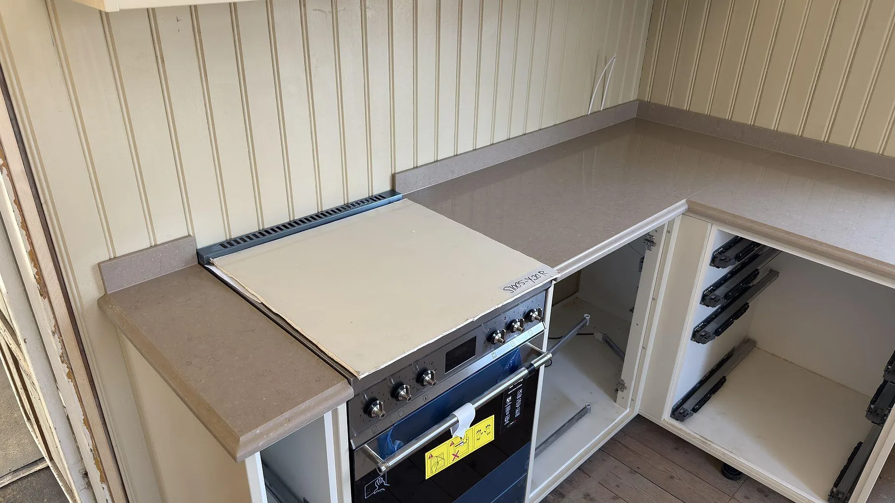 Hörn av köksbänk i beige Silestone Coral Clay med fristående spis infogad i bänkraden i ett kök i Valla, Katrineholm.