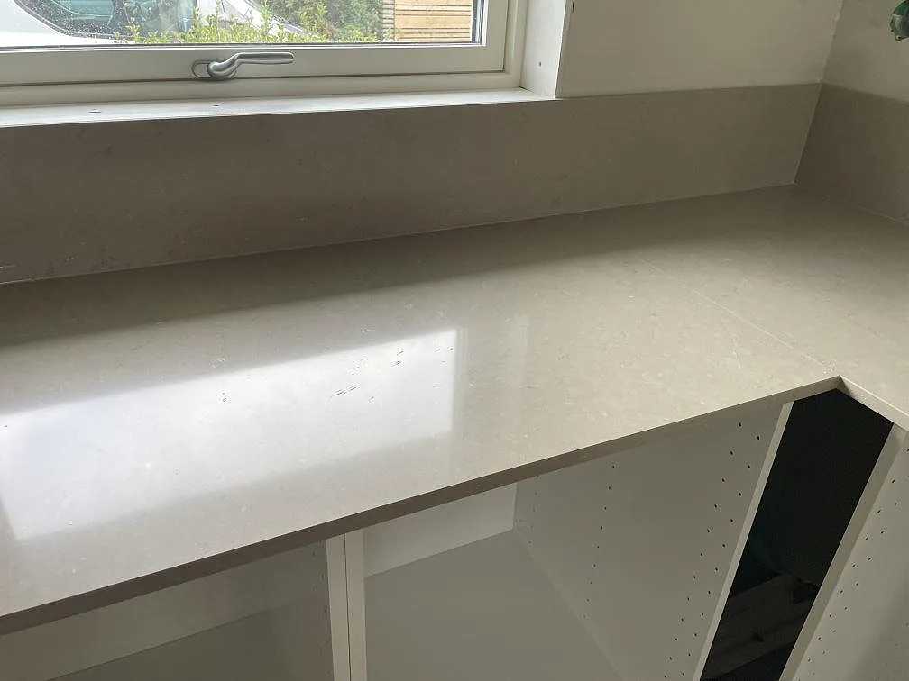 Rak köksbänk i varm gråbeige Silestone Coral Clay, polerad, under fönster i Varberg.