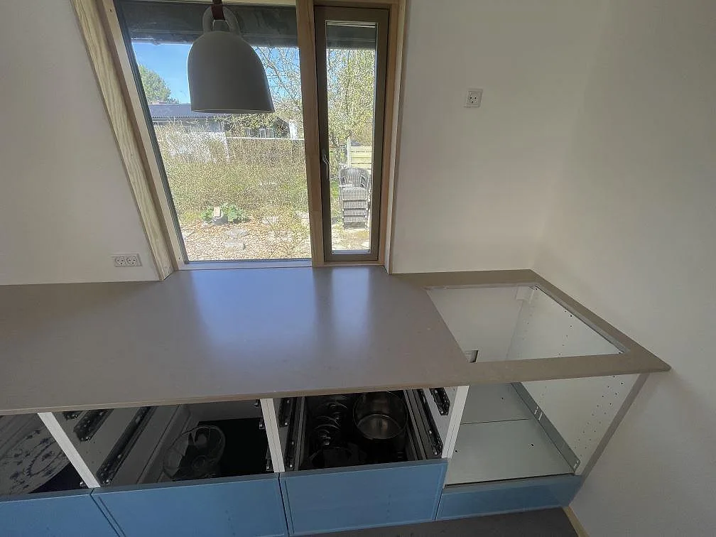 Hörnparti av köksbänkskiva i matt Silestone Coral Clay med öppna stommar under montering längs en fönstervägg i ett kök i Vejby Strand.