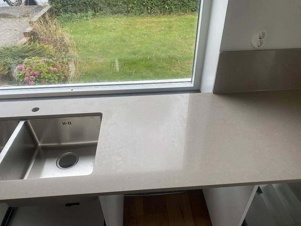 Polerad Silestone Coral Clay bänkskiva med underlimmad dubbel rostfri diskho framför fönstret i ett kök i Vellinge.