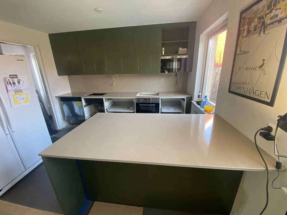 U-format kök med köksbänkskiva i Silestone Coral Clay, polerad greige kompositsten, mot gröna luckor och köksö i Vellinge.