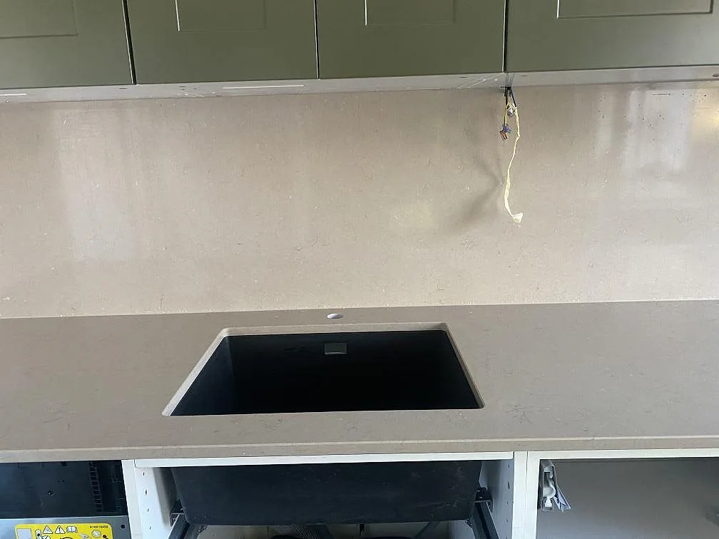 Underlimmad svart kompositdiskho i en köksbänkskiva i polerad Silestone Coral Clay i ett kök i Vellinge.