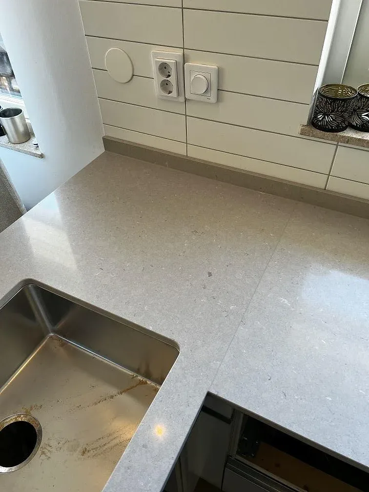Närbild på underlimmad rostfri diskho och vit kakelvägg intill en bänkskiva i Silestone Coral Clay i Vellinge.