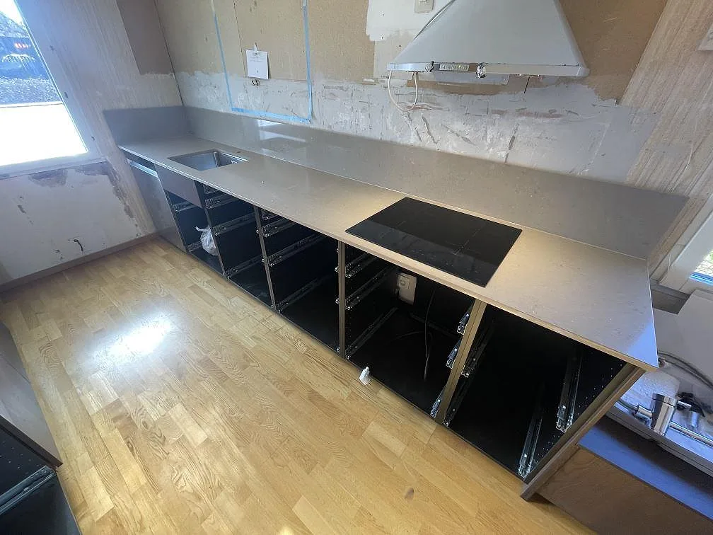 Köksbänkskiva i beige Silestone Coral Clay, polerad, med underlimmad rostfri diskho och infälld induktionshäll längs väggen i ett kök under montering i Vendelsö.