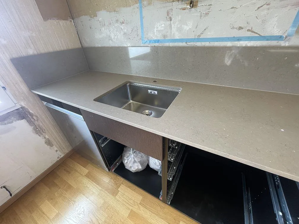 Underlimmad rostfri diskho i en polerad Silestone Coral Clay köksbänkskiva med uppvikt stänkkant i ett kök i Vendelsö.