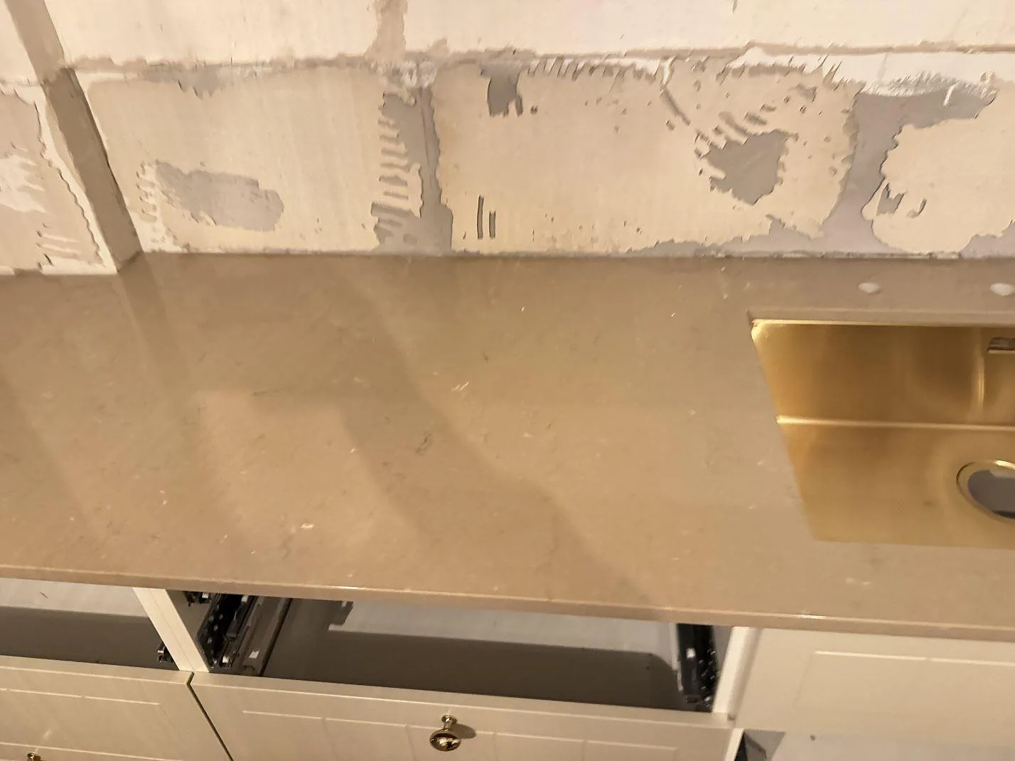 Köksbänkskiva i Silestone Coral Clay med polerad yta, guldfärgad diskho och öppna lådor i Ystad.