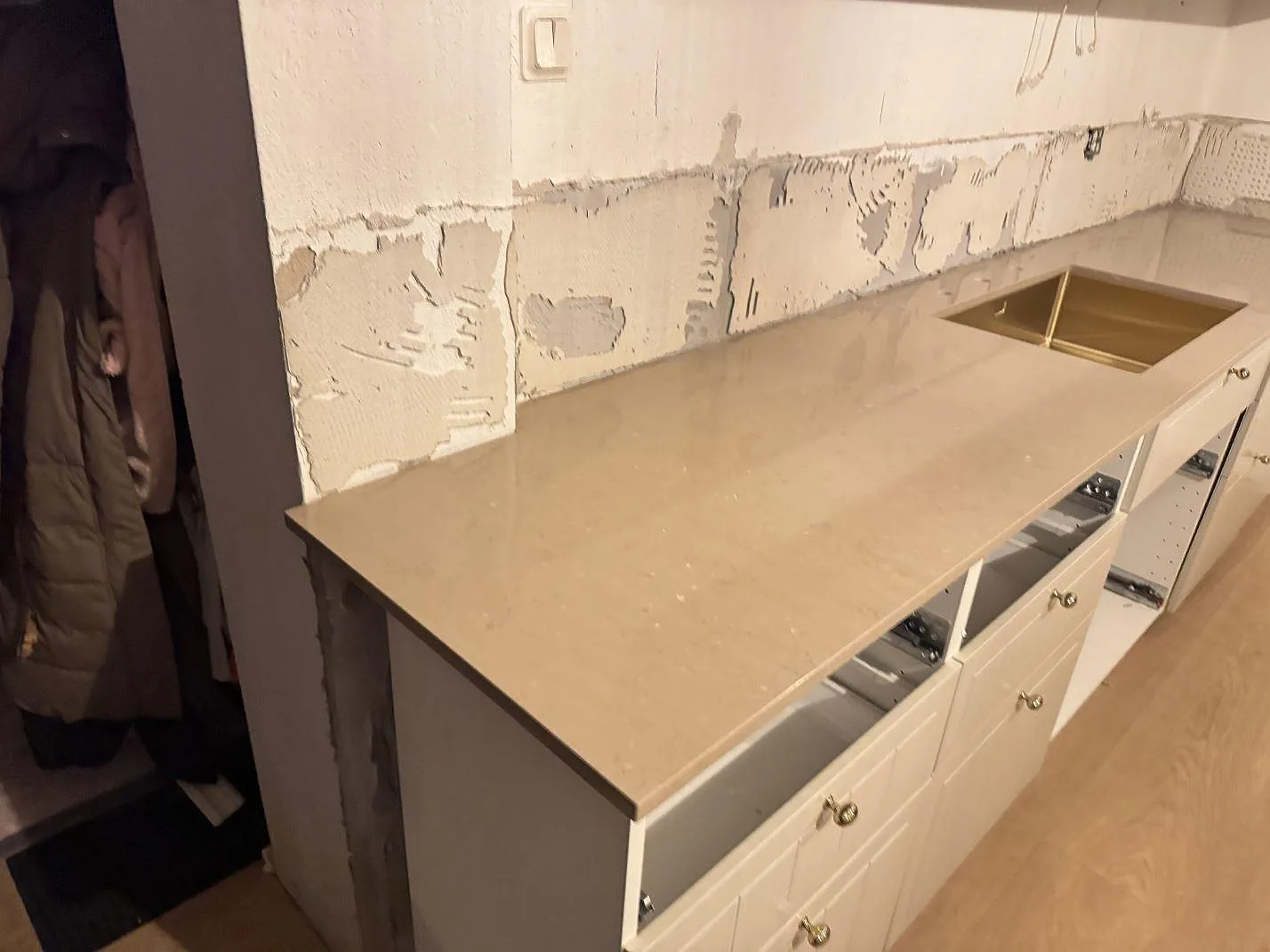 Lång köksbänkskiva i 20 mm polerad Silestone Coral Clay med guldfärgad diskho under montering i Ystad.