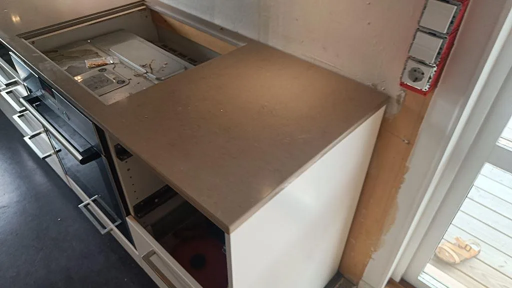 Närbild av höger bänkdel i polerad Silestone Coral Clay med hällöppning under montering i Ytterby.