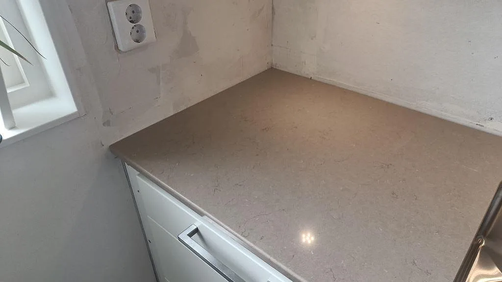 Hörnsektion av polerad Silestone Coral Clay vid fönster och diskho i köket i Ytterby.