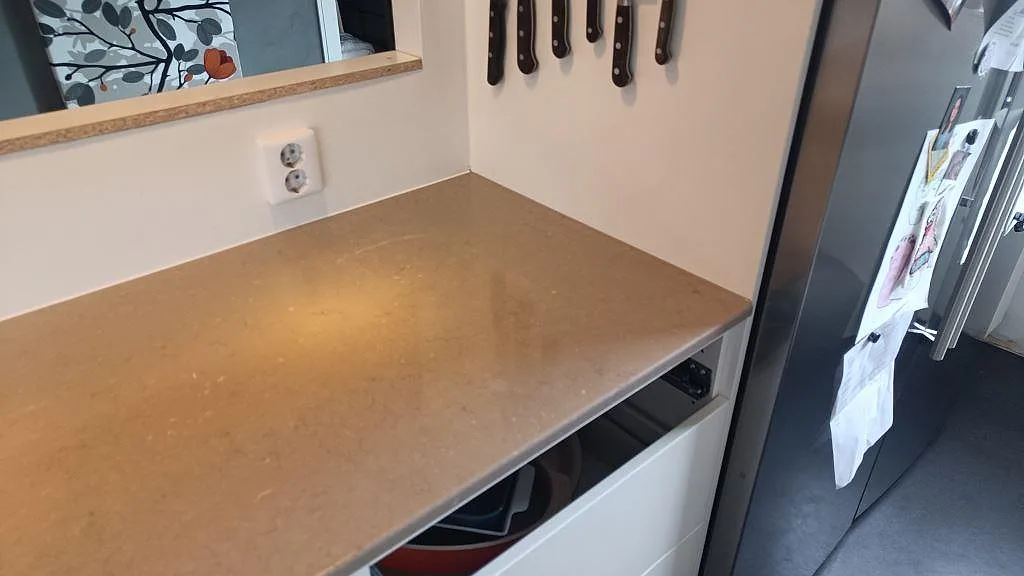 Sidobänk i polerad Silestone Coral Clay med varm gråbeige yta och vägguttag i köket i Ytterby.