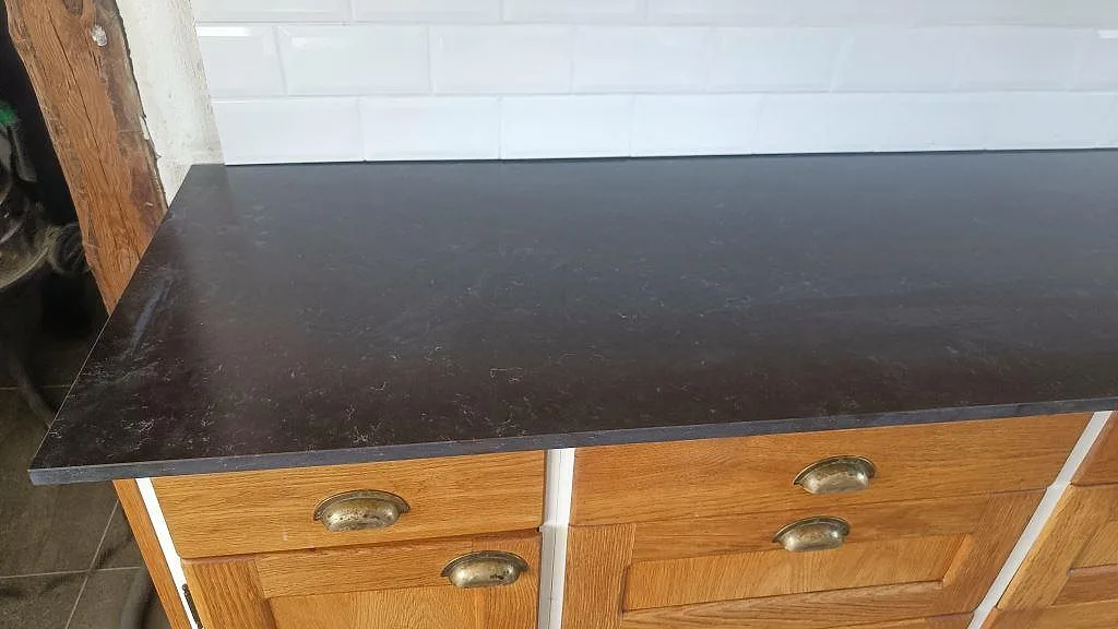 Rak detaljbild av mörk köksbänkskiva i Silestone Corktown, Mocka, på träinredning med vit kakelvägg i Blentarp.