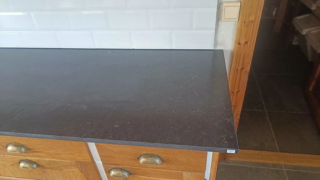Detalj av hörn och framkant på köksbänkskiva i Silestone Corktown, Mocka, mot vit kakelvägg i Blentarp.