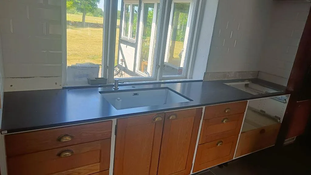 Köksbänkskiva i mörk Silestone Corktown, Mocka, med vit underlimmad diskho och urtag för häll i ett kök i Blentarp.