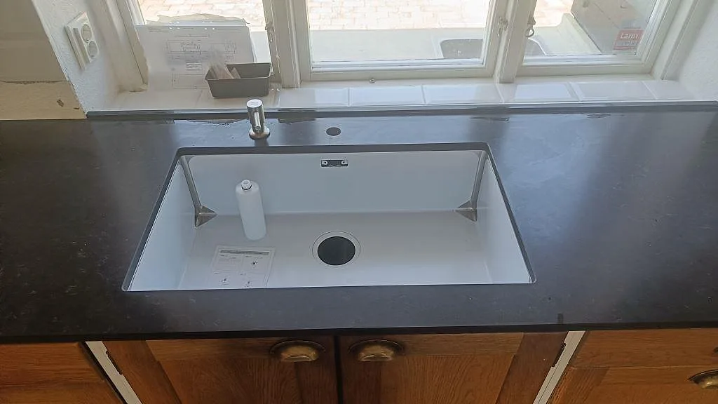 Detalj av vit underlimmad diskho i köksbänkskiva av Silestone Corktown, Mocka, framför fönster i Blentarp.