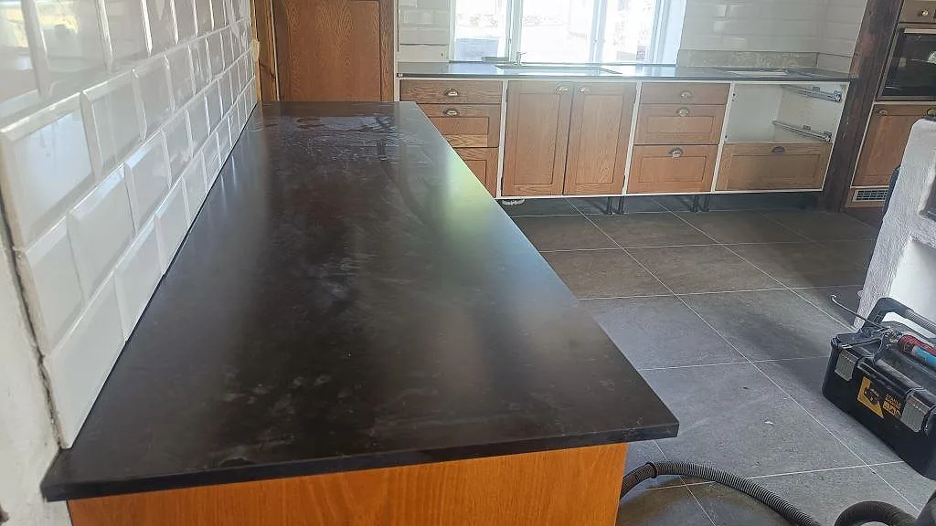 Bred vy över köksbänkskiva i mörk Silestone Corktown, Mocka, på träinredning med kaklad vägg i Blentarp.