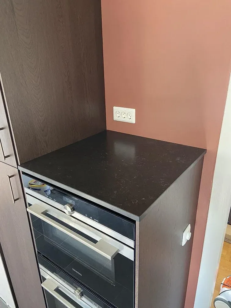 Köksbänkskiva och matchande stänkkant i svart Silestone Corktown ovanför Siemens-ugnar i ett kök i Gråbo.