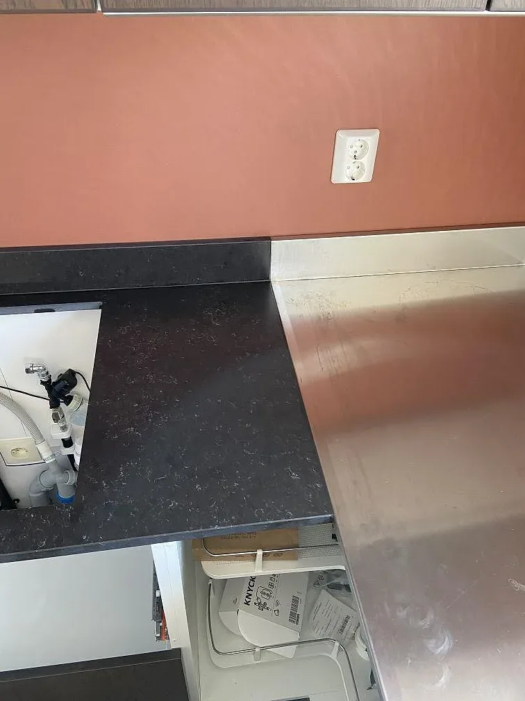 Köksbänkskiva i mörk Silestone Corktown med förberedd diskhoplats och rostfritt stänkskydd i ett kök under montering i Gråbo.