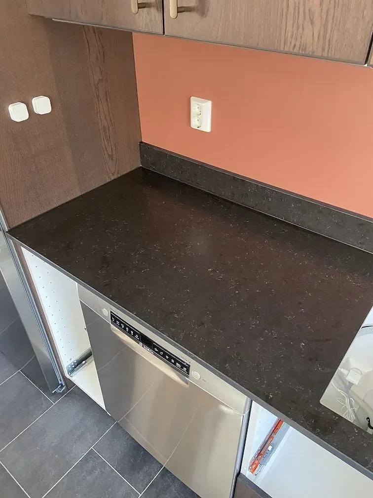 Mörk matt Silestone Corktown köksbänkskiva med synlig speckel-ådring och rostfritt stänkskydd i ett kök i Gråbo.