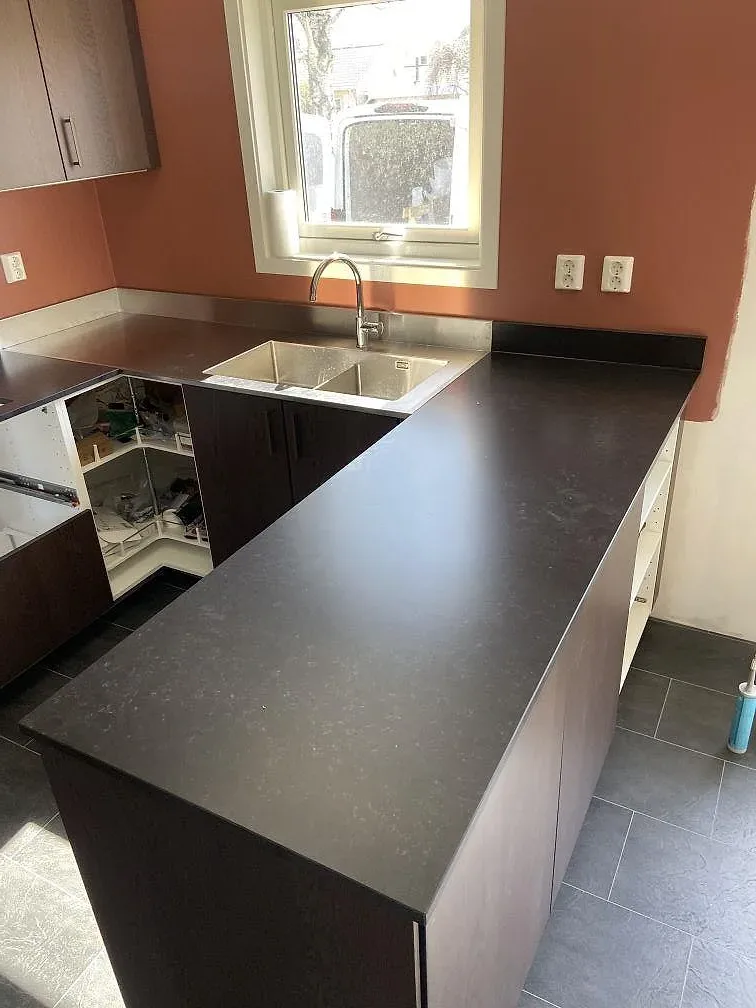 Köksbänkskiva i mörk matt Silestone Corktown mot terrakottavägg, med rostfritt stänkskydd och fönster i ett kök i Gråbo.