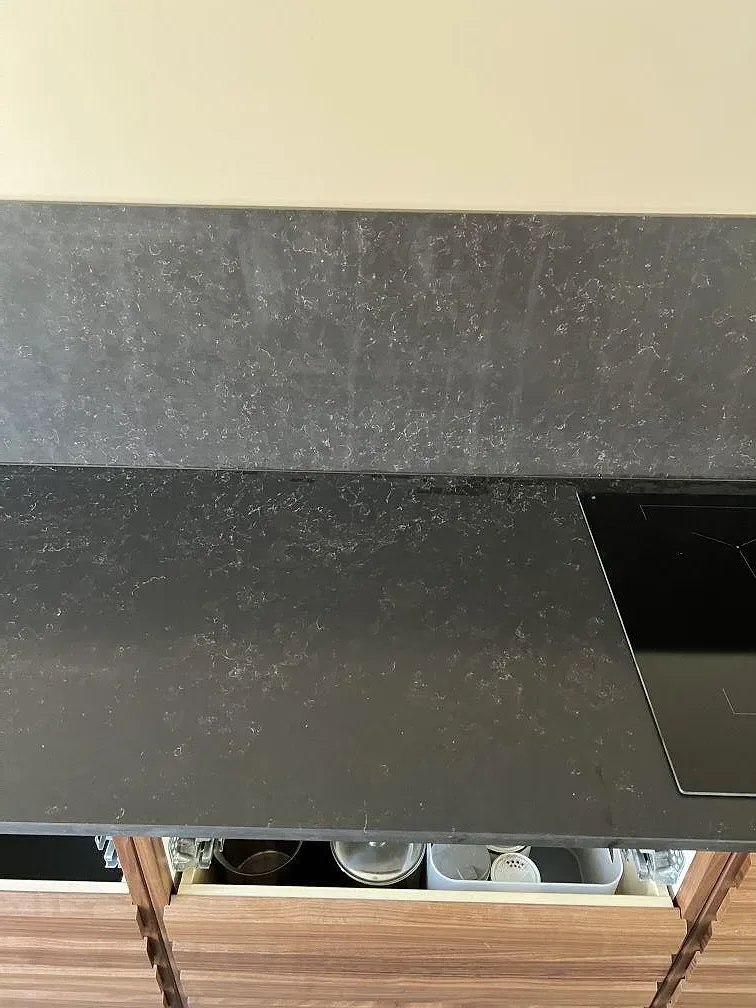 Detalj av mörk Silestone Corktown-bänkskiva i matt finish intill hällzon och träinredning i Lomma.