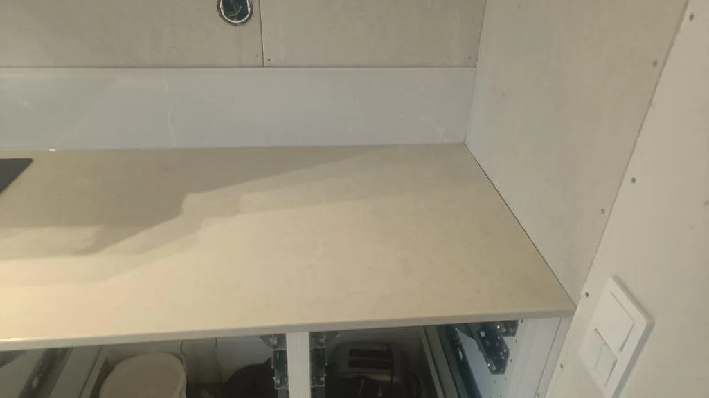 Höger del av köksbänkskiva i polerad Silestone Desert Silver med ljus stänkkant och vita stommar i Ängelholm.