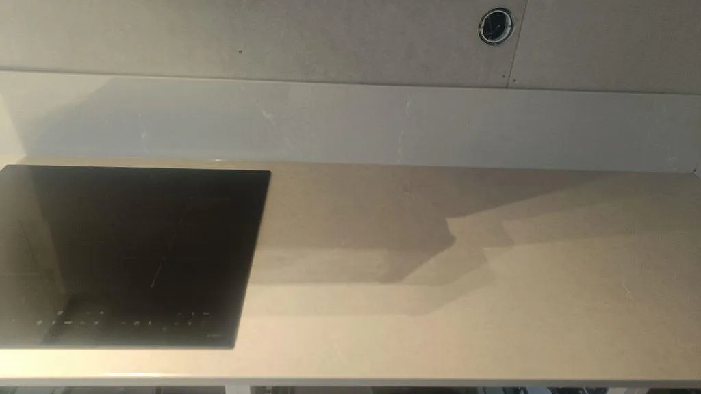 Närbild på polerad Silestone Desert Silver runt svart häll och uppvikt stänkkant i kök i Ängelholm.