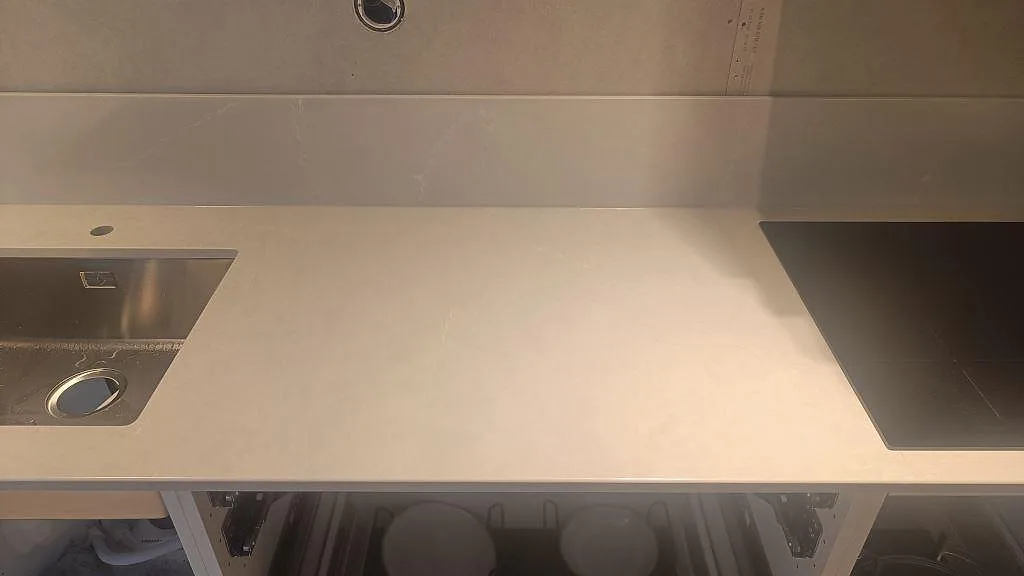 Detalj av polerad Silestone Desert Silver med underlimmad rostfri diskho, blandarhål, svart häll och stänkkant i Ängelholm.