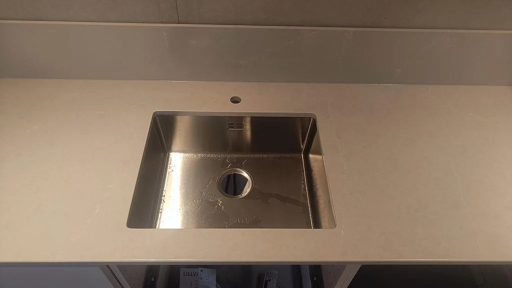 Underlimmad rostfri diskho i polerad Silestone Desert Silver med blandarhål och låg stänkkant i ett kök i Ängelholm.
