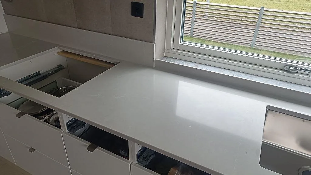 Polerad köksbänkskiva i Silestone Desert Silver med rektangulärt urtag, rostfri diskho och öppna köksstommar i Ängelholm.