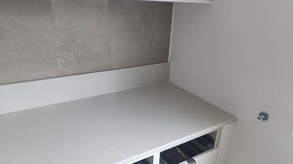 Rak köksbänkskiva i Silestone Desert Silver, polerad grå kvartskomposit, med matchande stänkskydd mot grå väggplattor i Ängelholm.