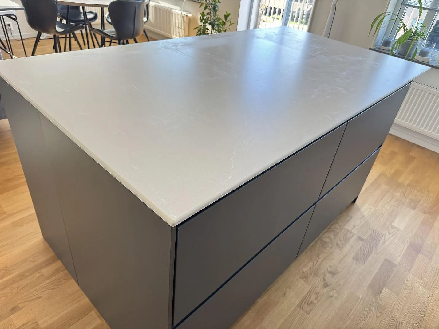 Köksö med bänkskiva i ljusgrå Silestone Desert Silver kvartskomposit, matt Mocka, över mörkgrå köksluckor i ett kök i Alingsås.