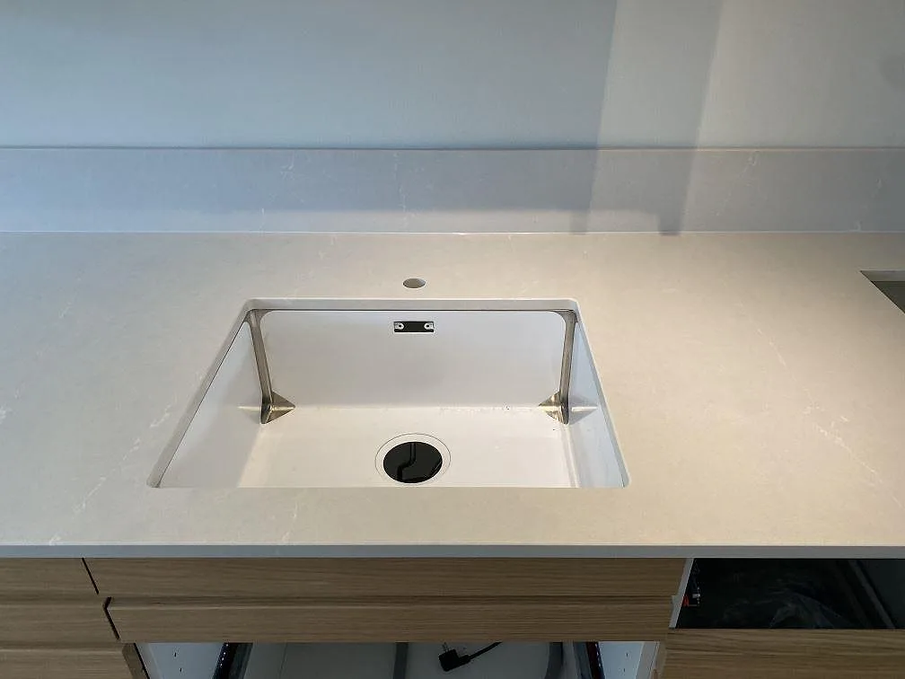 Detalj av polerad Silestone Desert Silver vid diskhoområdet, låg stänkkant och ljus ådring i köket i Halmstad.