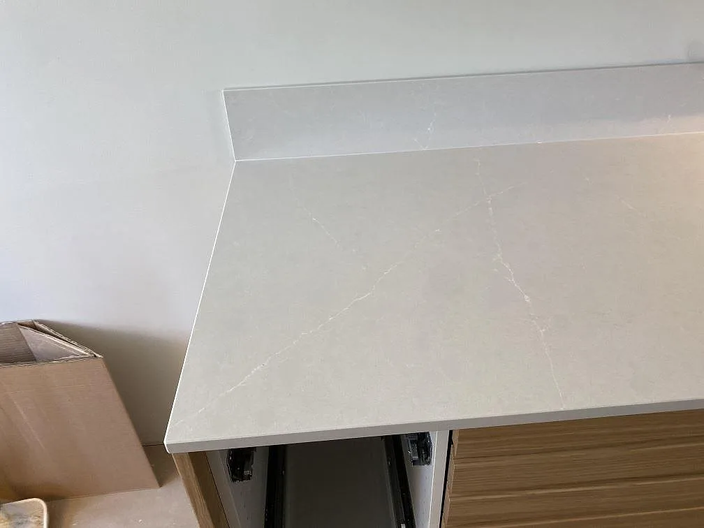 Hörndetalj av köksbänkskiva i polerad Silestone Desert Silver med låg stänkkant och öppna stommar under montering i Halmstad.