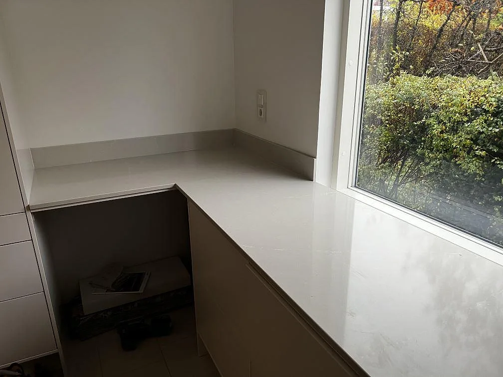 L-formad köksbänkskiva i polerad Silestone Desert Silver komposit vid ett stort fönster i Halmstad.