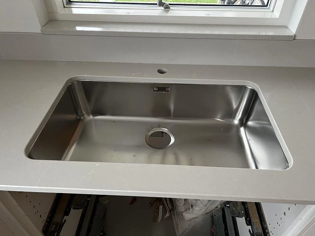 Närbild på polerad Silestone Desert Silver bänkskiva med rostfri diskho och uppvikt kant i ett kök i Halmstad.