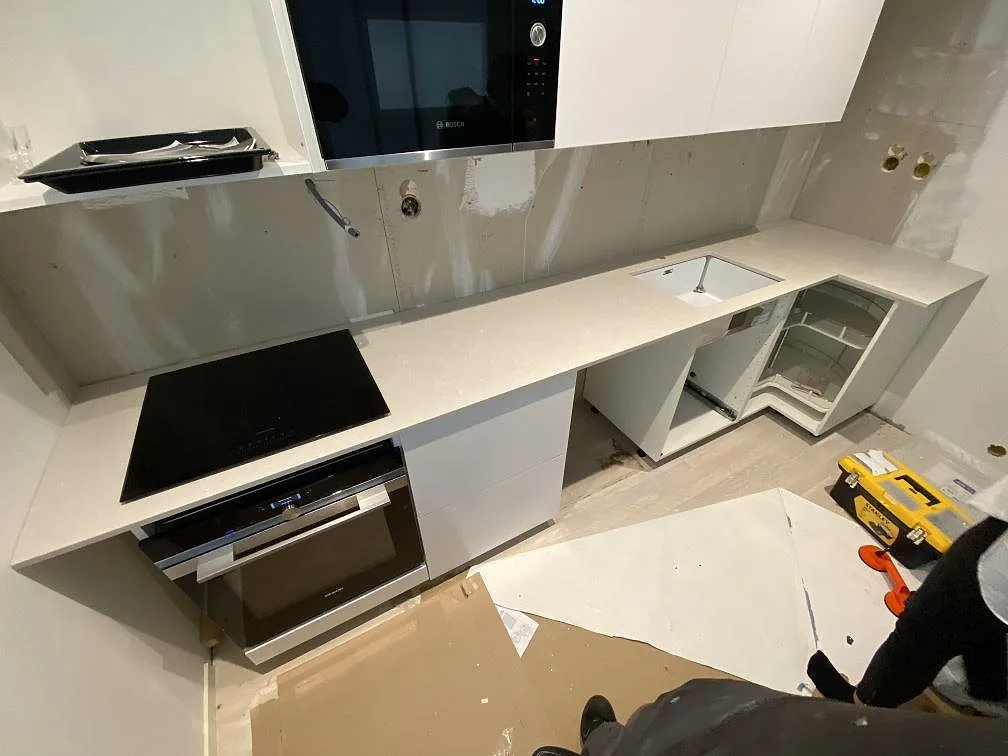 Köksbänkskiva i Silestone Desert Silver, ljus grå kvartskomposit, i ett L-format kök i Höllviken med infälld induktionshäll och underlimmad diskho under montering.