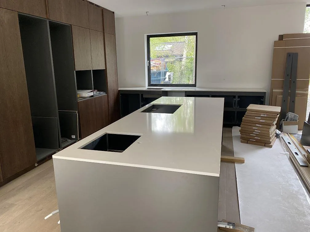 Köksö med polerad bänkskiva i Silestone Desert Silver, underlimmad rostfri diskho och hällurtag i ett kök under montering i Höllviken.
