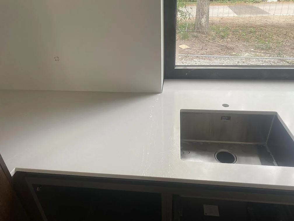 Bänkyta i polerad Silestone Desert Silver vid fönster med underlimmad rostfri diskho i kök under montering i Höllviken.